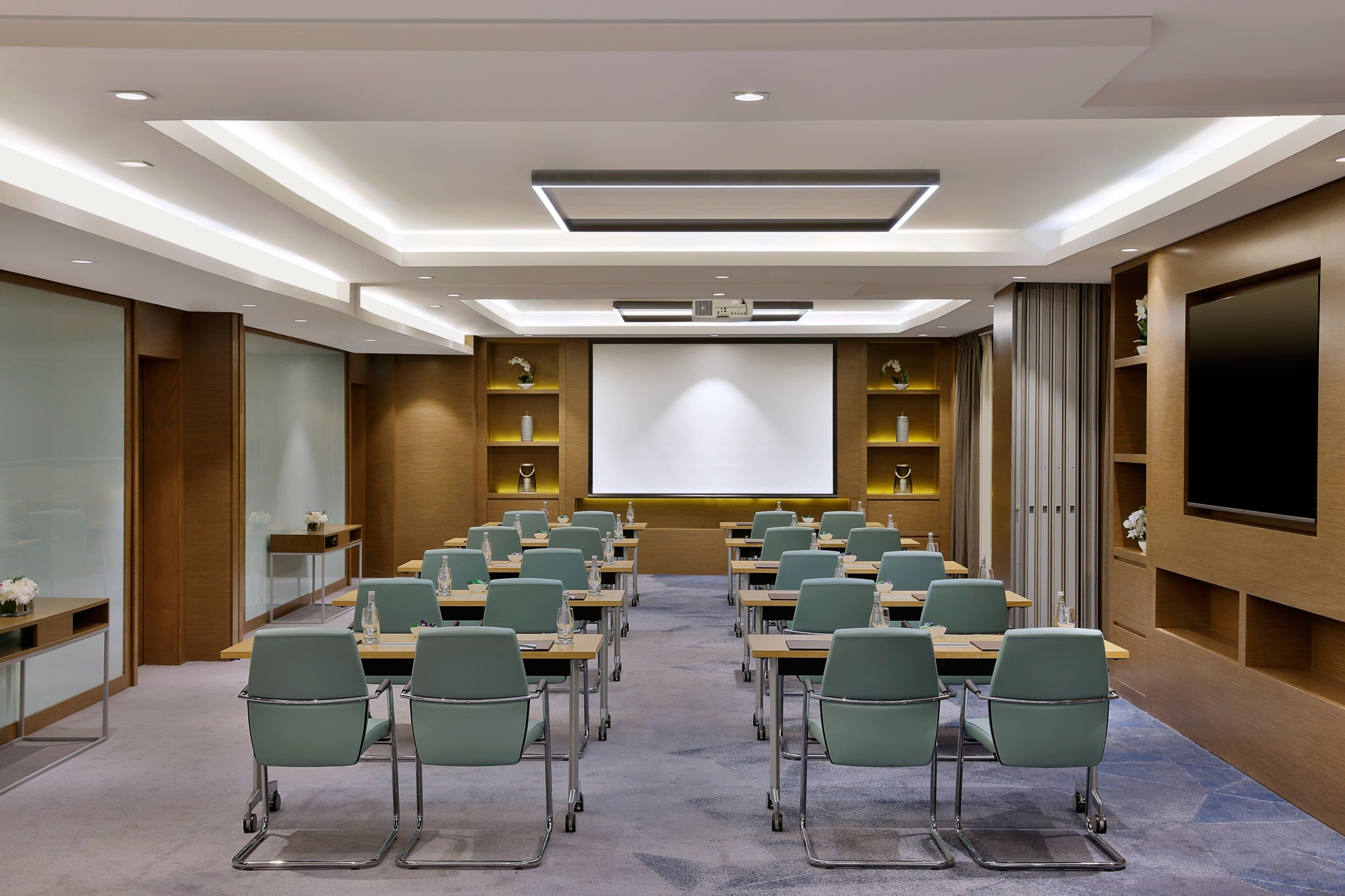 Un salón de conferencias con una pantalla grande, filas de sillas y un proyector.