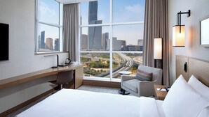 Habitación de hotel con un ventanal grande que ofrece vistas a la ciudad, una cama, un escritorio y una silla.