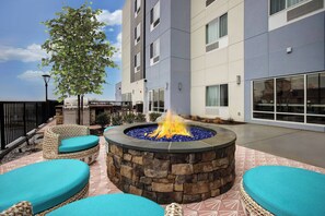 A fire pit surrounded by wicker furniture with cushions, set on a patio with a stone wall. - TownePlace Suites by Marriott Potomac Mills Woodbridge (Woodbridge)
