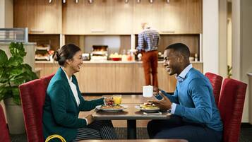 A couple dining in a modern hotel restaurant with a kitchen in the background.