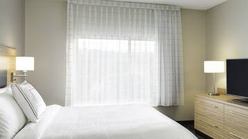 Una habitación de hotel con una cama grande, dos lámparas de noche, un televisor de pantalla plana, un aparador de madera y cortinas translúcidas.