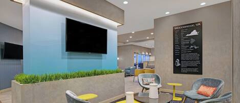 A modern lounge area with comfortable seating, a flat-screen TV, and a wall-mounted information board.