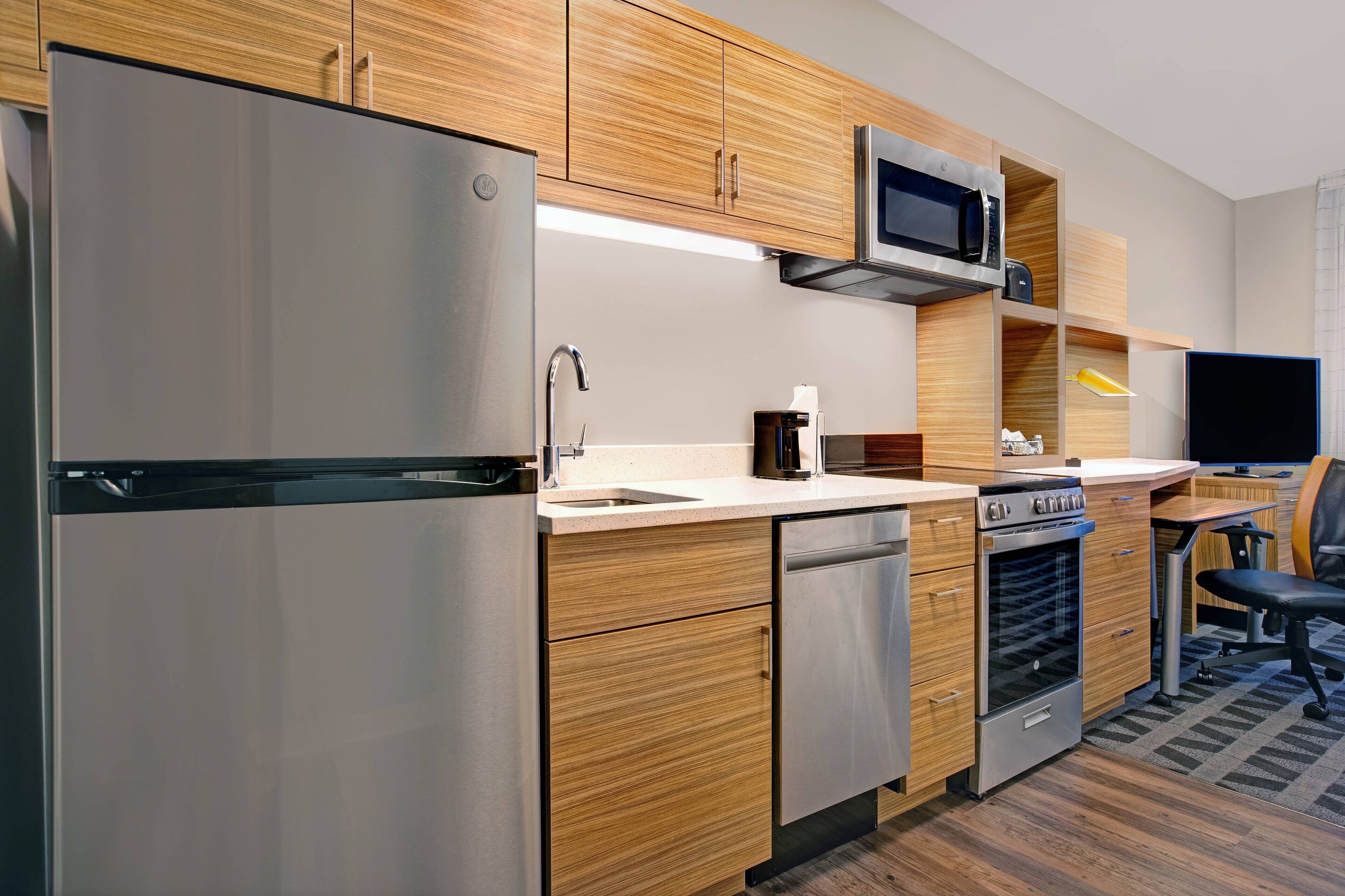 Une cuisine moderne dotée d’appareils électroménagers en acier inoxydable, de meubles en bois et d’un four à micro-ondes encastré.