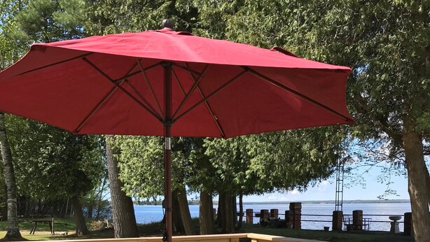 A wooden deck with a table and chairs under a red umbrella, overlooking a body of water.