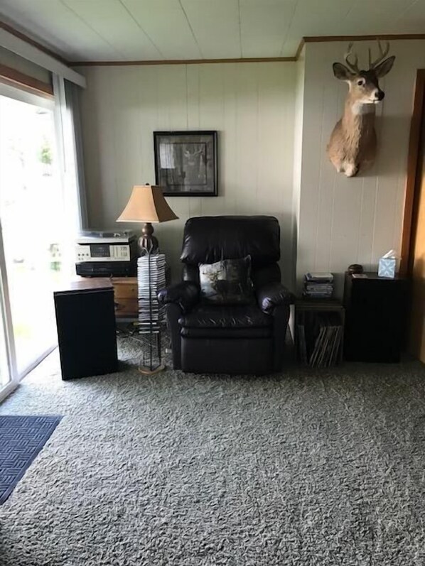Un salon avec un fauteuil en cuir, une lampe, une tête de cerf montée sur un support et un tableau encadré accroché au mur.