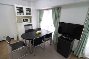 A small room with a dining table, chairs, a microwave, a TV, and a cabinet with dishes.