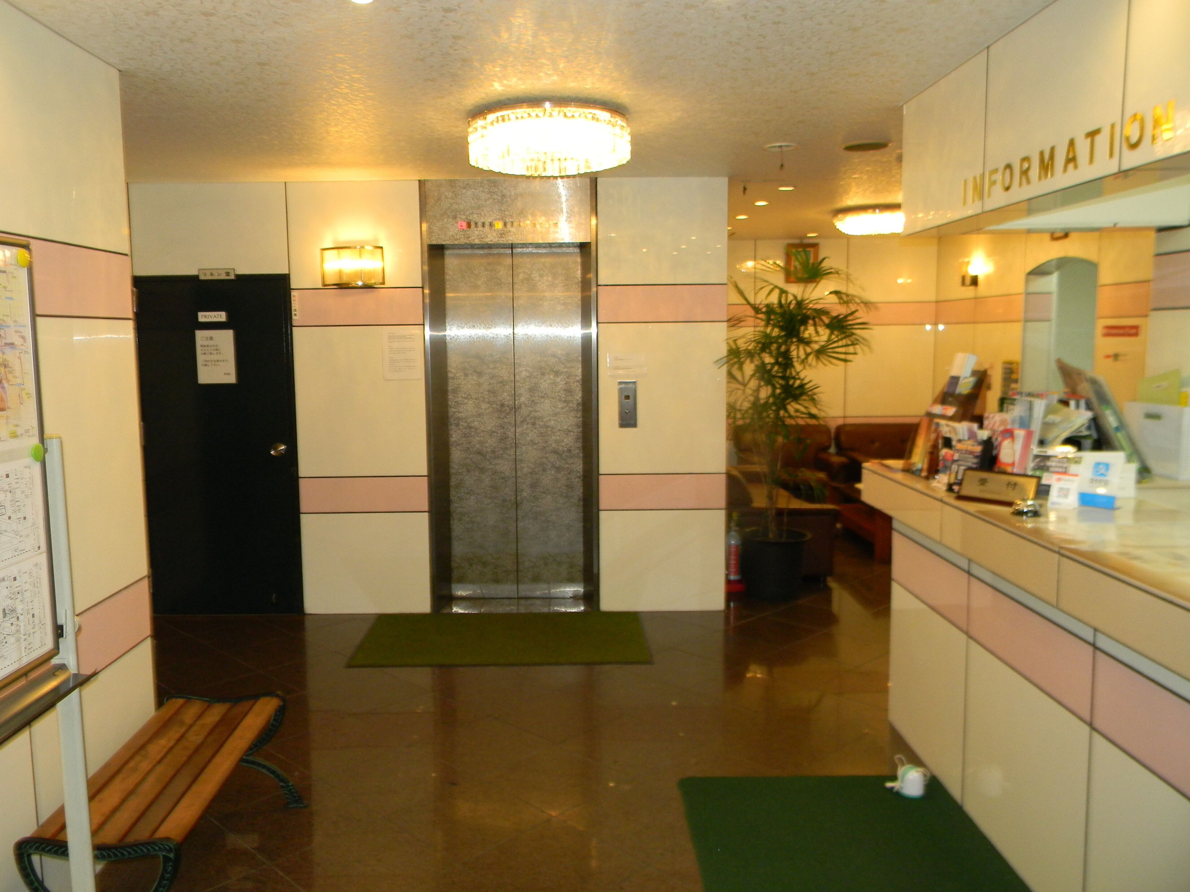 A hotel lobby with a reception desk, a bench, an elevator, and a sign labeled "INFORMATION".