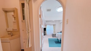 A hallway leading to a bedroom with a bed, a bedside table, and a window with curtains. - Weekly Green In Namba (Osaka)