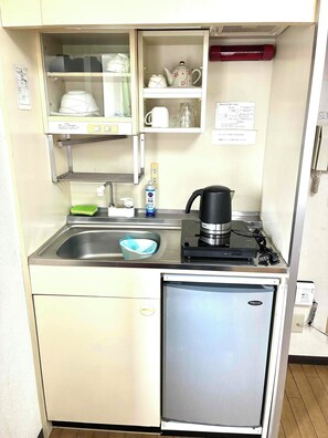 A compact kitchenette with a sink, a small refrigerator, a coffee maker, and a glass cabinet containing kitchenware.