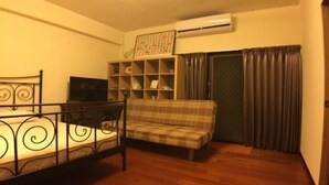 A room with a bed, a sofa, a TV, a shelf with various items, and an air conditioning unit. - Penghu Happy Fish (Magong)