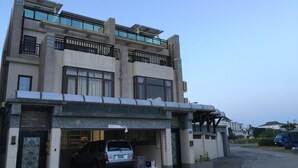 A multi-story building with a garage entrance, a parked car, and a blue vehicle in the background. - Penghu Happy Fish (Magong)