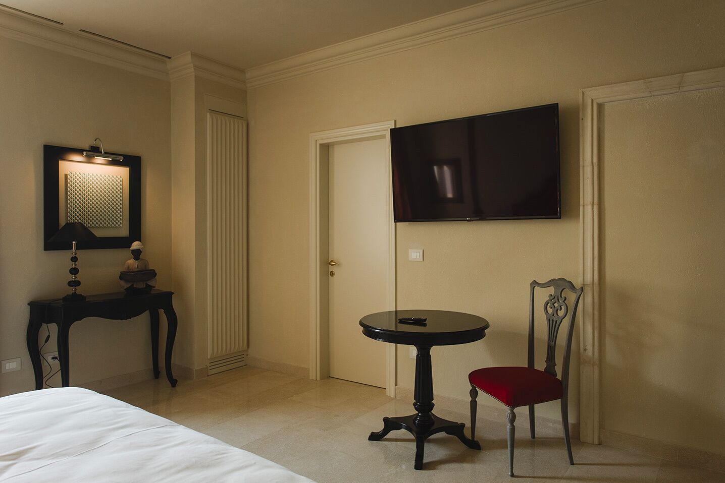 Een hotelkamer met een bed, een klein rond tafeltje met een stoel, een aan de muur bevestigde televisie en een decoratieve lamp.