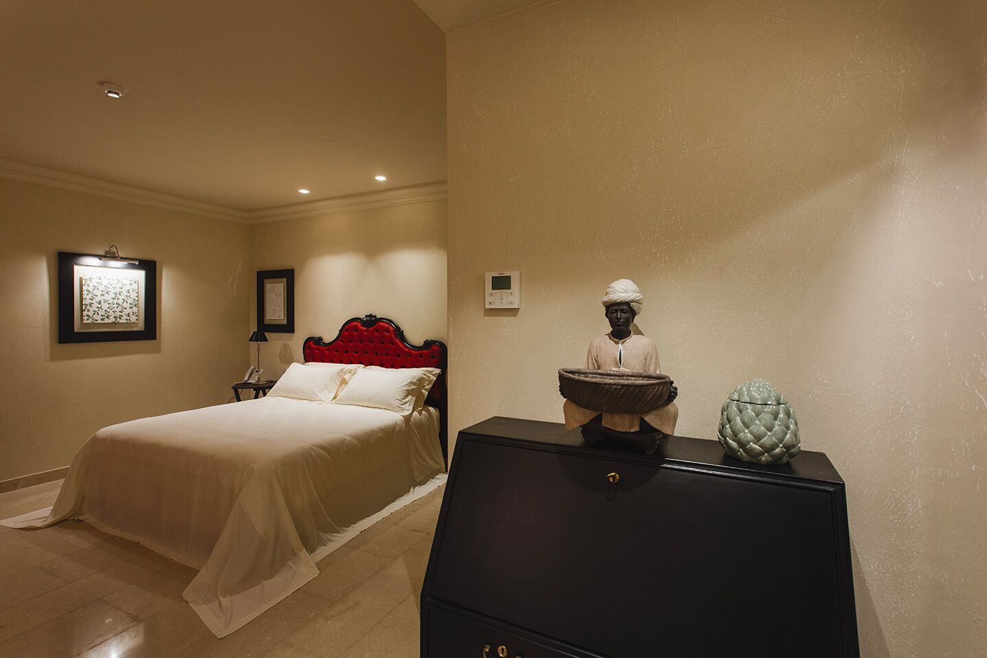 A hotel room with a bed, a nightstand, a dresser, and a wall-mounted thermostat.