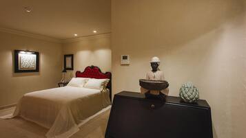 A hotel room with a bed, a nightstand, a dresser, and a wall-mounted thermostat.