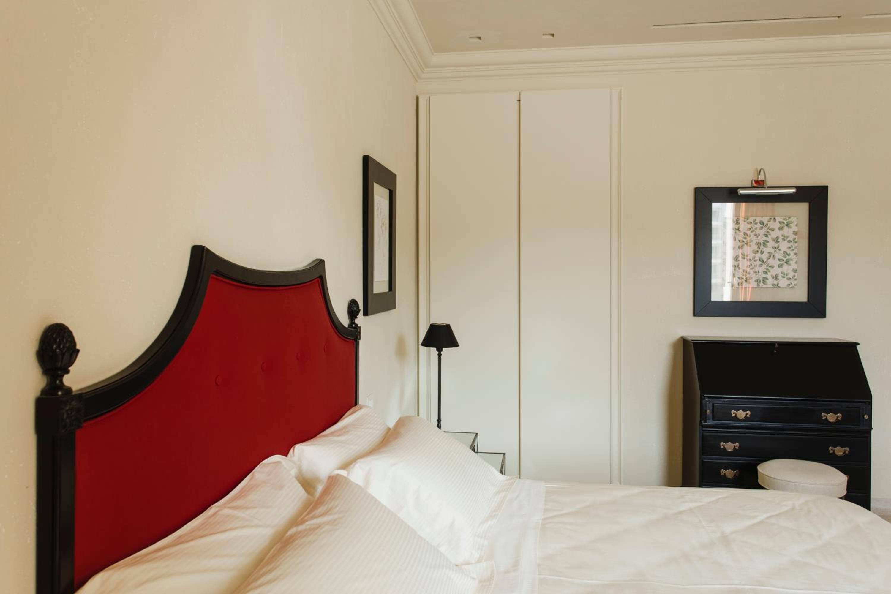 A neatly made bed with a red headboard, a bedside lamp, and a dresser with drawers.