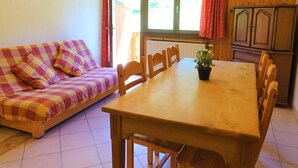 A room with a wooden dining table, a sofa, and a window with curtains. - Ski-in/Ski-out Apartment, 2-Bedroom, Sleeps 6 with South Balcony and Parking (Arêches-Beaufort)