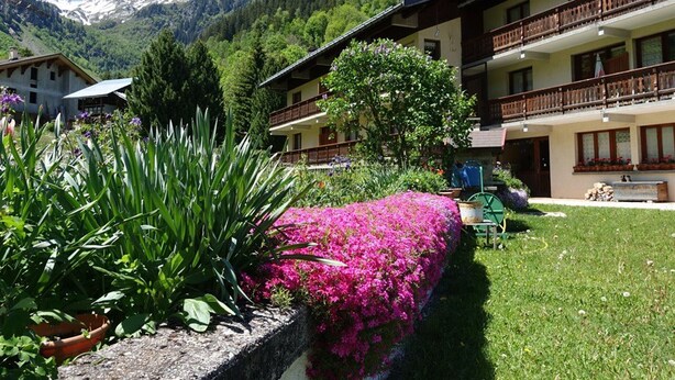 A hotel with a garden, a mountain view, and a balcony with wooden railings. - Ski-in/Ski-out Apartment, 2-Bedroom, Sleeps 6 with South Balcony and Parking (Arêches-Beaufort)