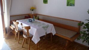 A dining area with a wooden table, four chairs, a bench, and a small table with a vase of flowers.