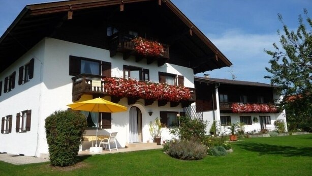 A two-story building with balconies adorned with red flowers, a yellow umbrella, and a small garden area.