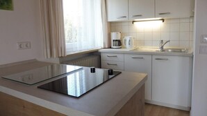 A compact kitchen with a glass-top island, white cabinets, a built-in oven, and a window with curtains.