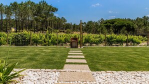 Un jardín cuidado con un sendero de piedra que lleva a una zona de estar, rodeado de una cerca y un viñedo al fondo.