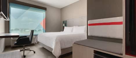 Une chambre d’hôtel avec un lit, un bureau, une chaise et une vue sur la ville.