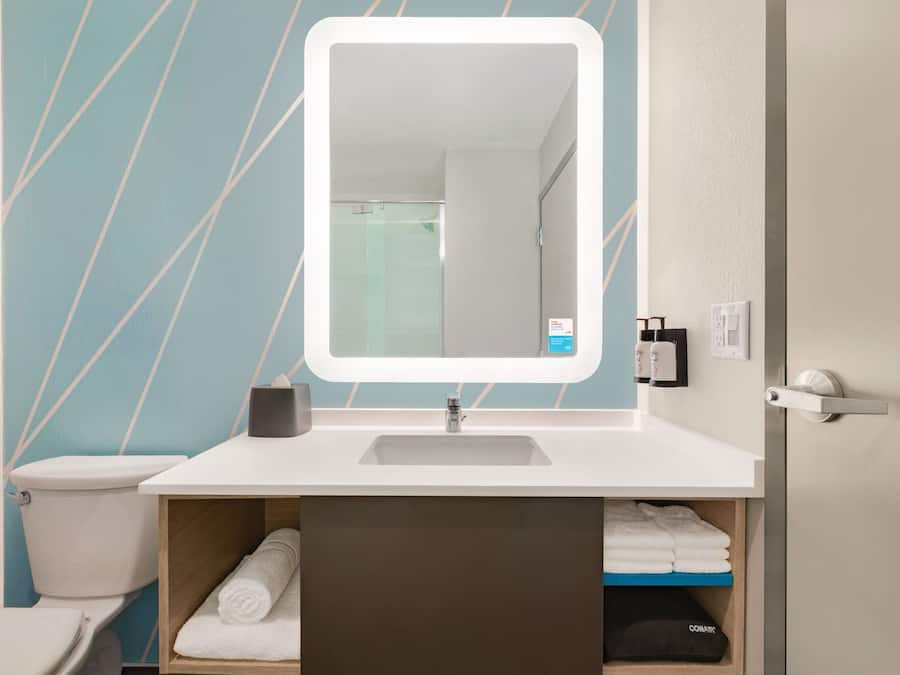 Un baño con un lavamanos blanco, un espejo y un toallero.