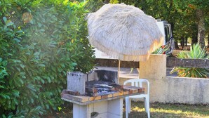 Ein Grillplatz mit einem Reetdach, einer Betonplatte und einem weißen Plastikstuhl.