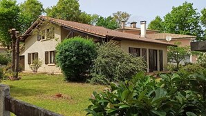 Ein zweistöckiges Haus mit einem Ziegeldach, umgeben von einem gepflegten Garten und Bäumen.