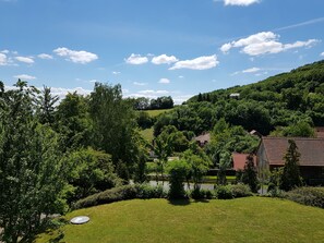 Un paysage verdoyant et luxuriant, avec un petit étang, entouré d’arbres et de quelques bâtiments aux toits rouges.