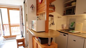 A compact kitchen with a microwave, sink, and a small refrigerator. There's a wooden cabinet and a window with a view of the outside. - Apartment for 5 with pool, balcony, close to ski and village (Arêches-Beaufort)