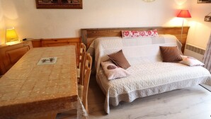 A cozy room with a wooden table, a bed with a white blanket and pillows, a wall clock, and a framed picture. - Apartment for 5 with pool, balcony, close to ski and village (Arêches-Beaufort)