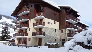 A multi-story chalet with wooden balconies and a stone facade, surrounded by snow-covered mountains. - Apartment for 5 with pool, balcony, close to ski and village (Arêches-Beaufort)