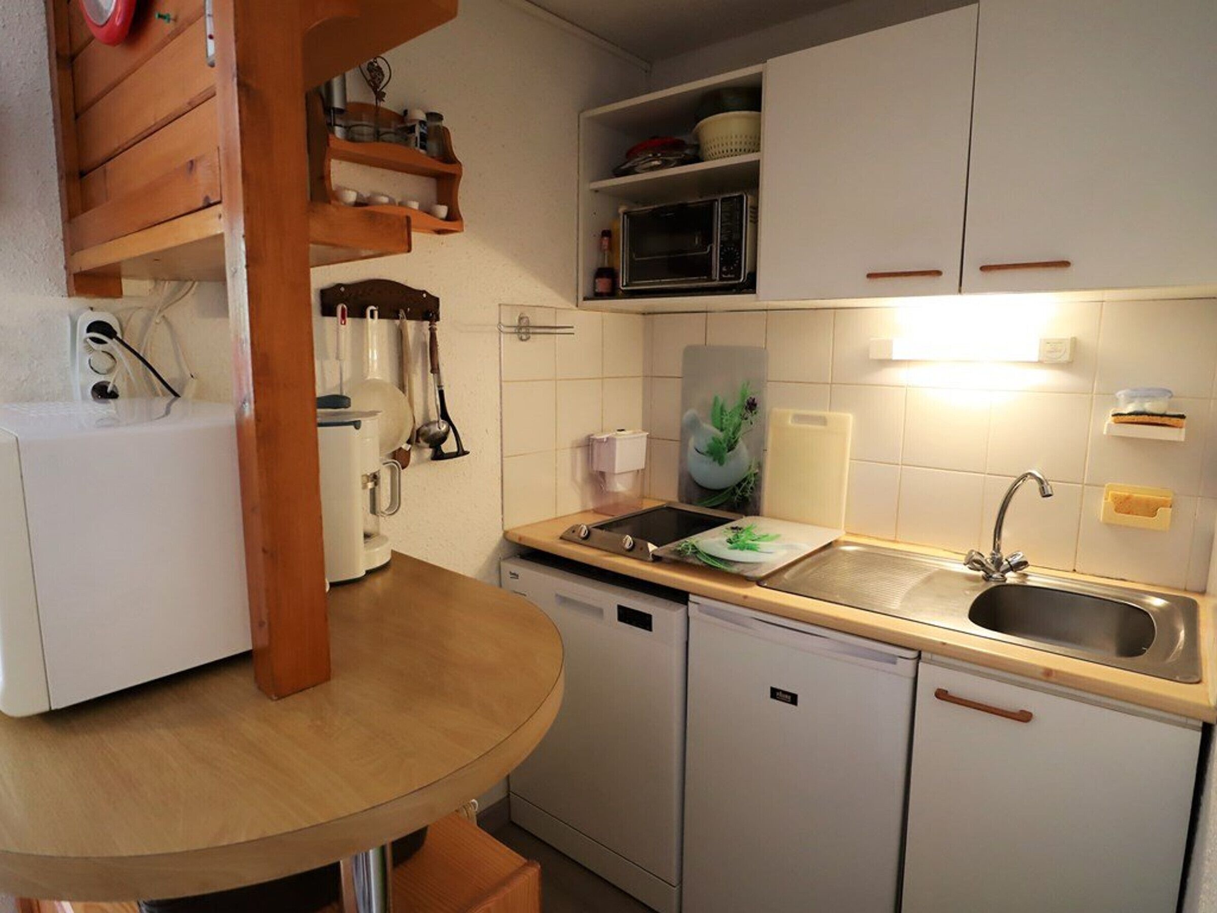 Cocina compacta con microondas, lavamanos y un refrigerador pequeño.