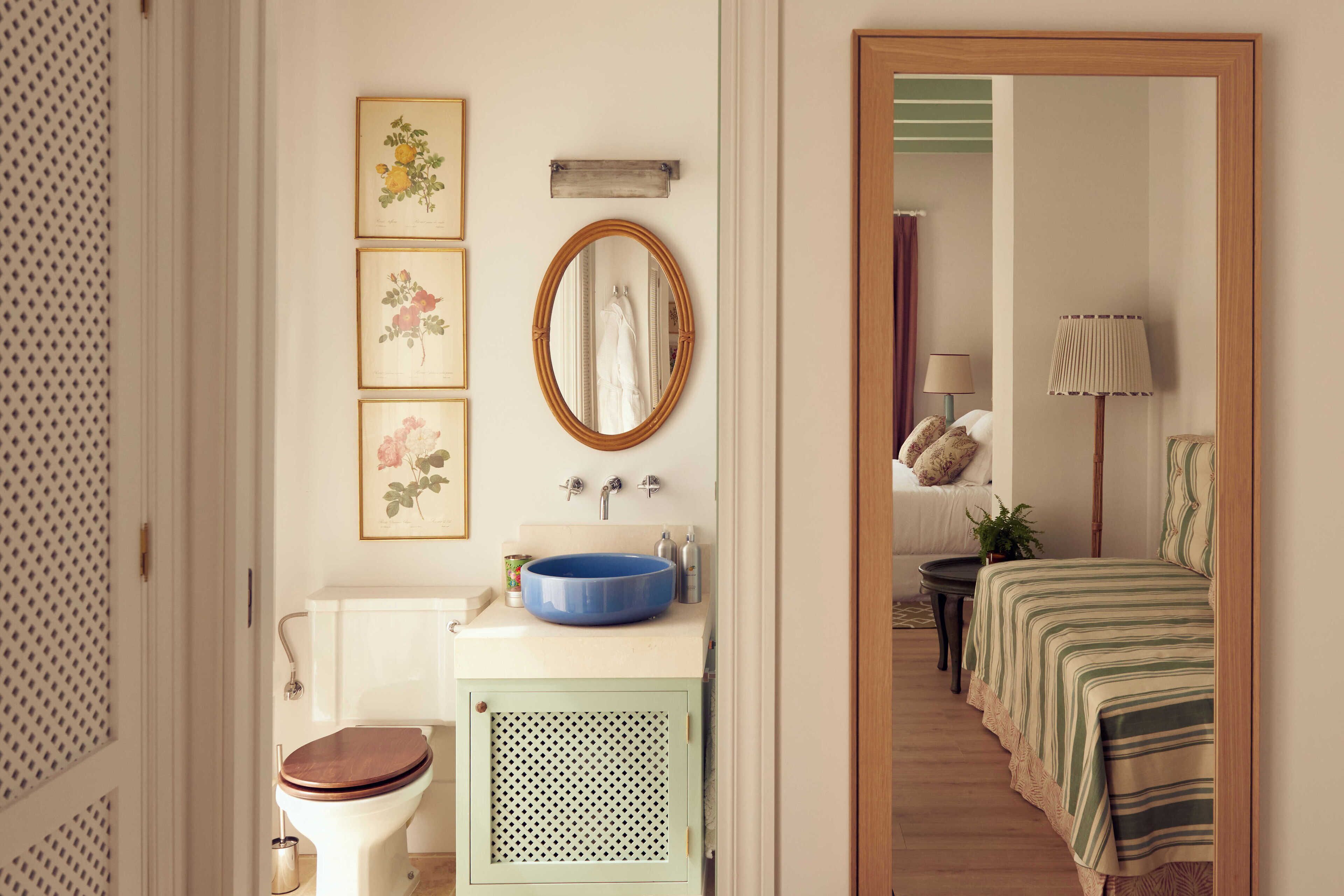 Un baño con inodoro, lavabo y espejo. Se observan cuadros enmarcados en la pared.