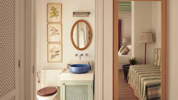 Un baño con inodoro, lavabo y espejo. Se observan cuadros enmarcados en la pared.