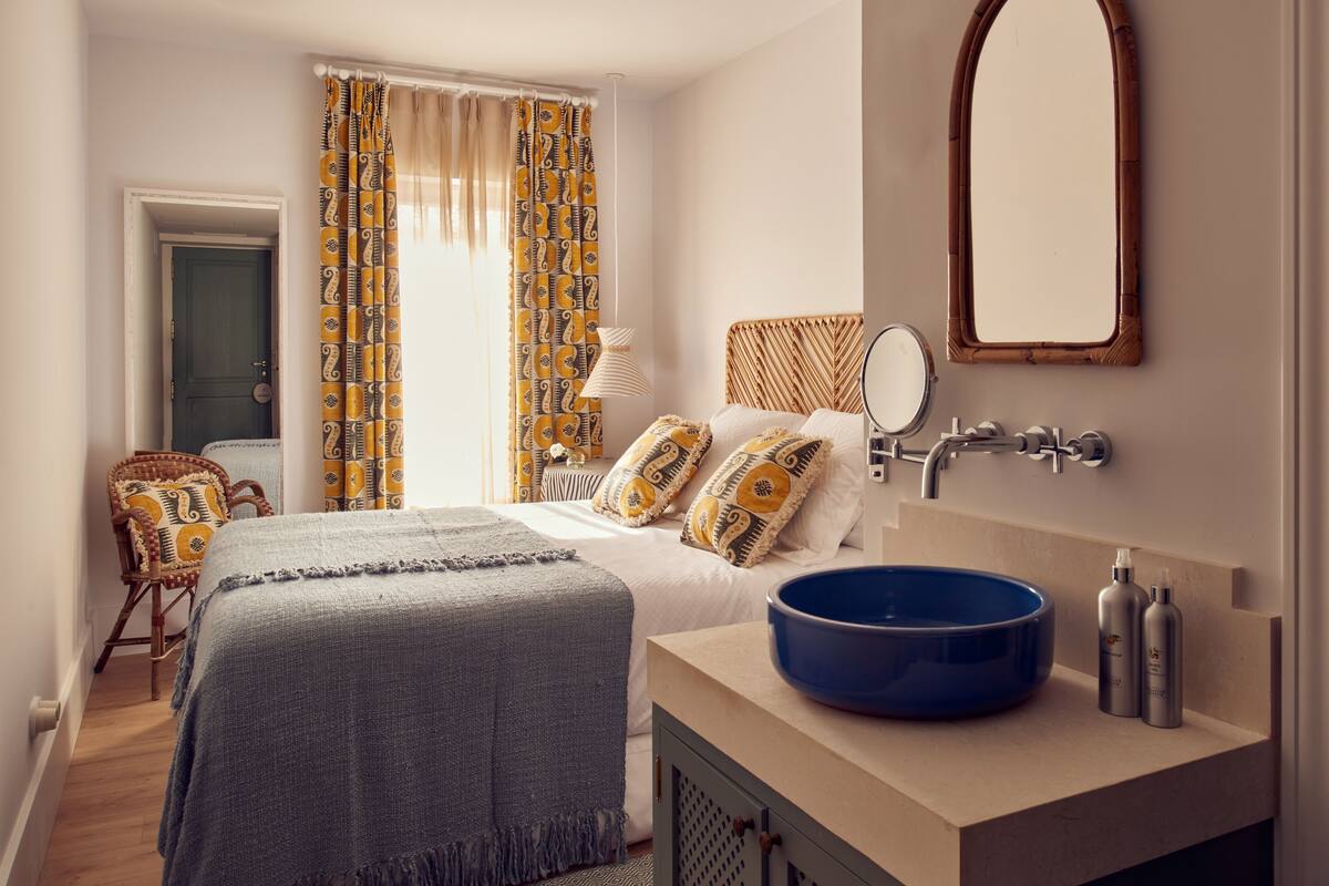A bedroom with a bed, a blue sink, a mirror, and a door.