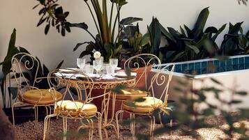 Una mesa redonda con sillas, rodeada de plantas en macetas y una pared de baldosas.