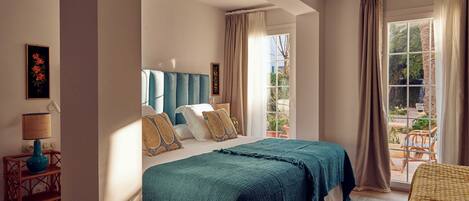 Un dormitorio con una cama grande, una mesita de noche con lámpara y vistas al exterior a través de una ventana.