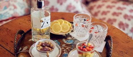 A tray with a bottle of gin, glasses of water with fruit, and plates of nuts and fruit salad.