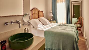 Une chambre d’hôtel avec une tête de lit en bois, un bol vert posé sur la commode, un lit recouvert d’une couverture verte et une chaise près de la fenêtre.