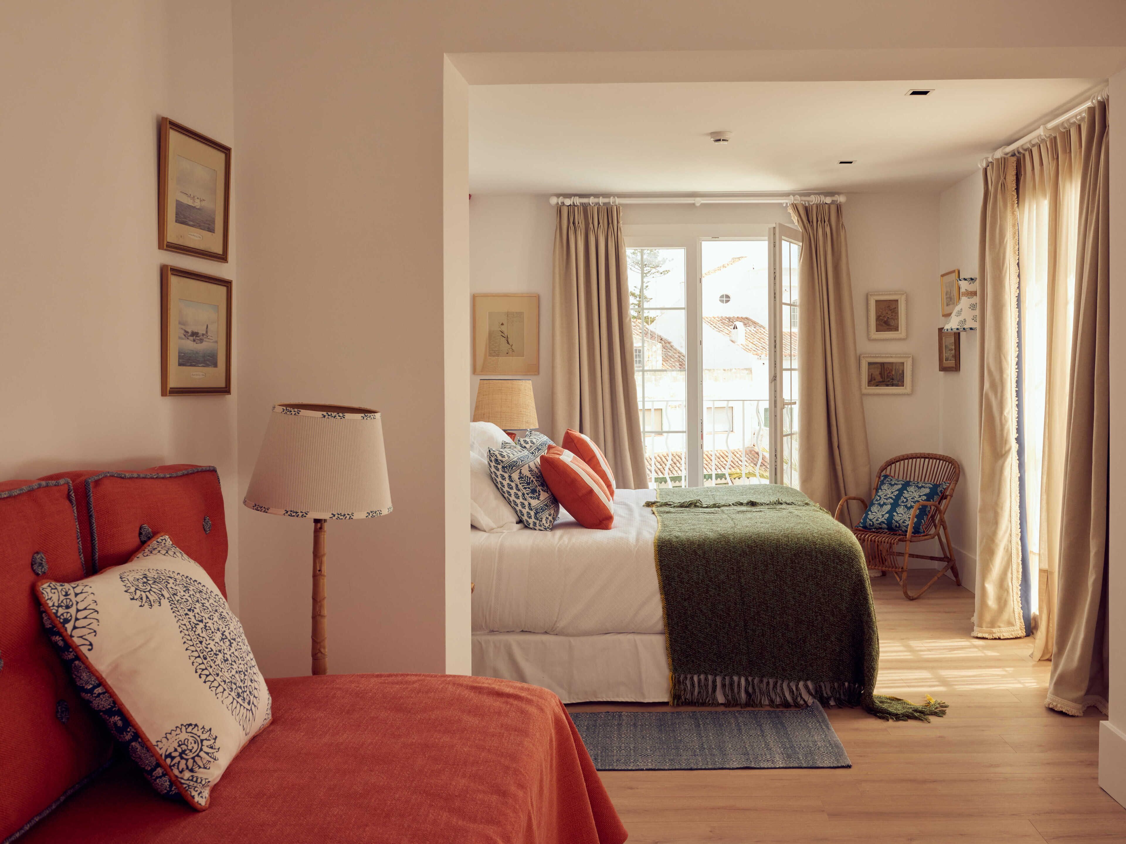 A bedroom with two beds, a chair, and a window with curtains.