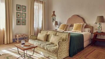 A bedroom with a bed, a sofa, a small table, and a lamp.