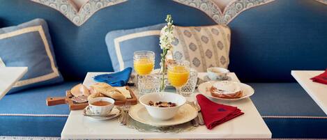 A breakfast setup on a sofa with a table, including orange juice, cereal, and a bowl of fruit.