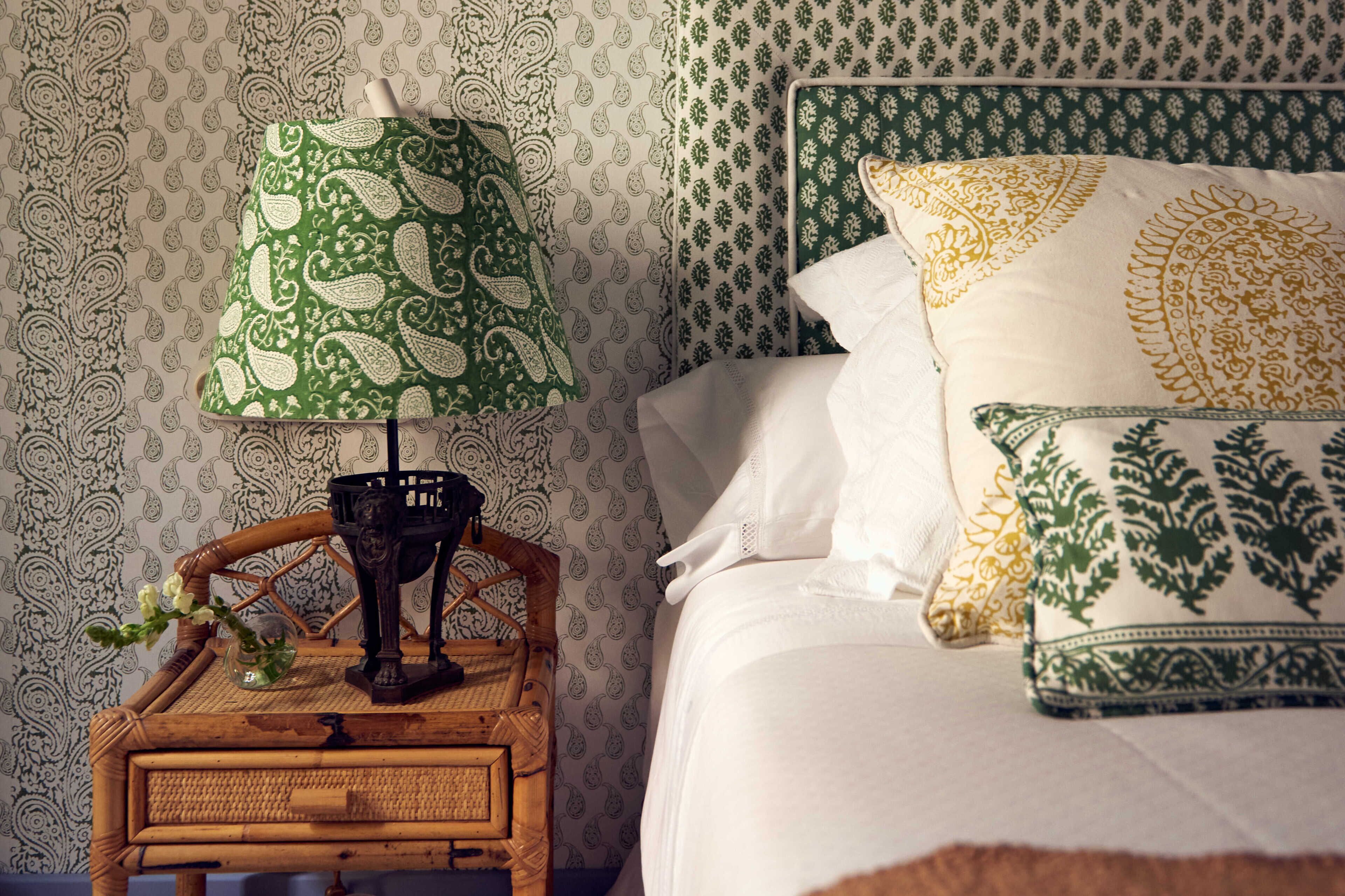 Una cama bien hecha con almohadas estampadas y una mesita de noche con una lámpara y objetos decorativos.