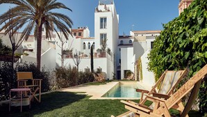 Un área de piscina con sillas de descanso, una palmera y un edificio con torre.