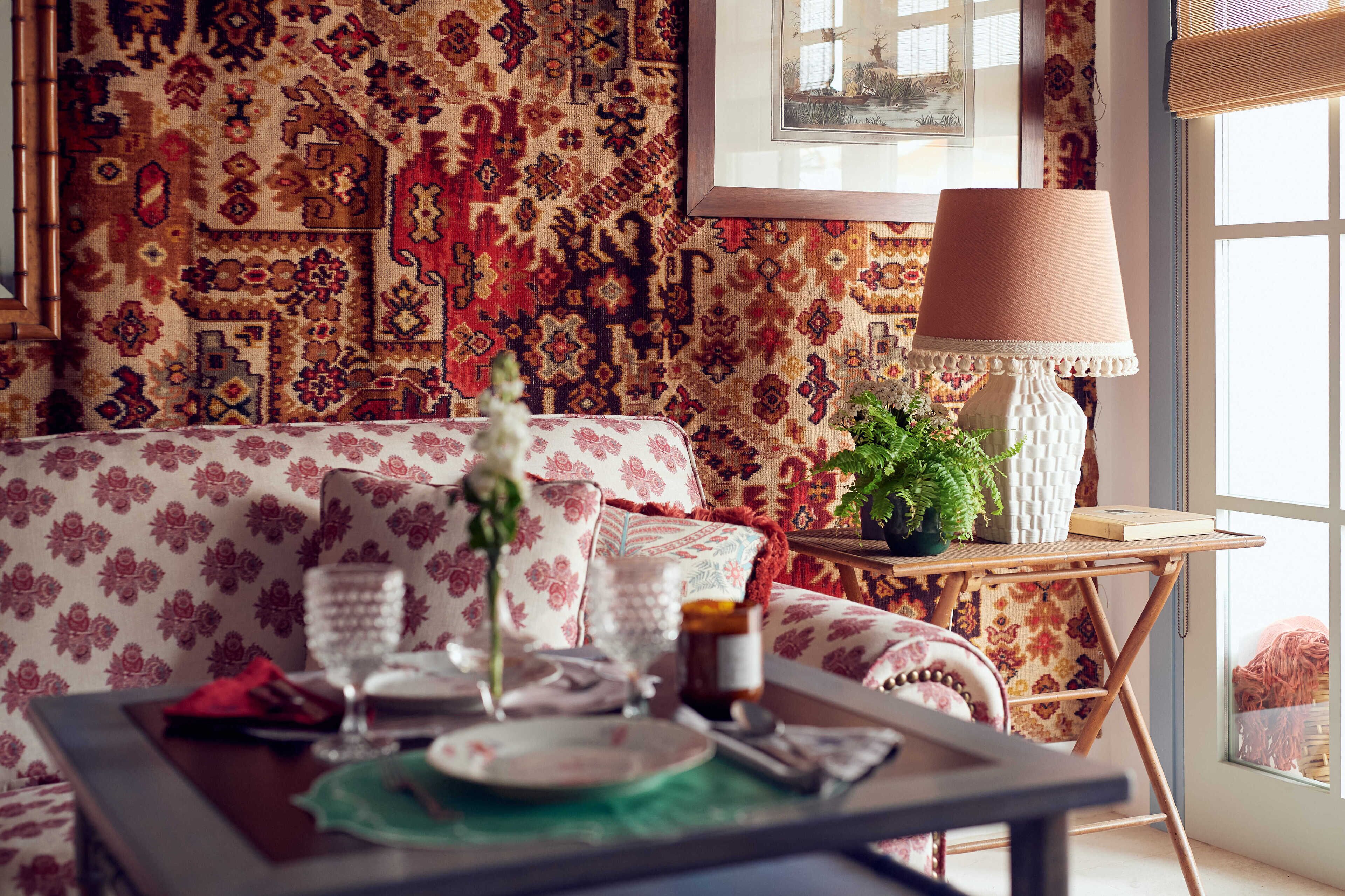 Un rincón comedor acogedor con una pared decorativa, un sofá, una mesa servida con platos, vasos y un jarrón.