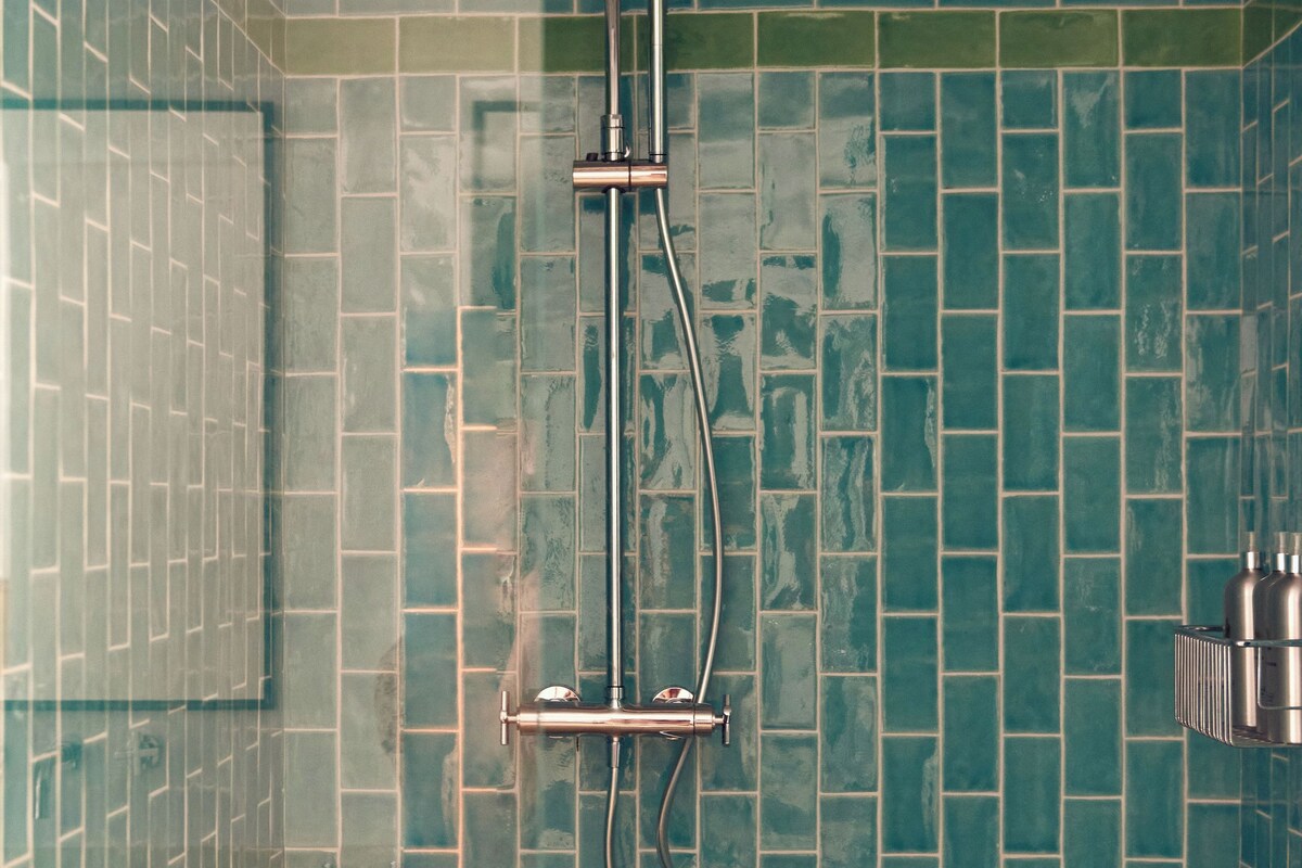 A bathroom with a shower, tiled walls, and a bed with a blanket.