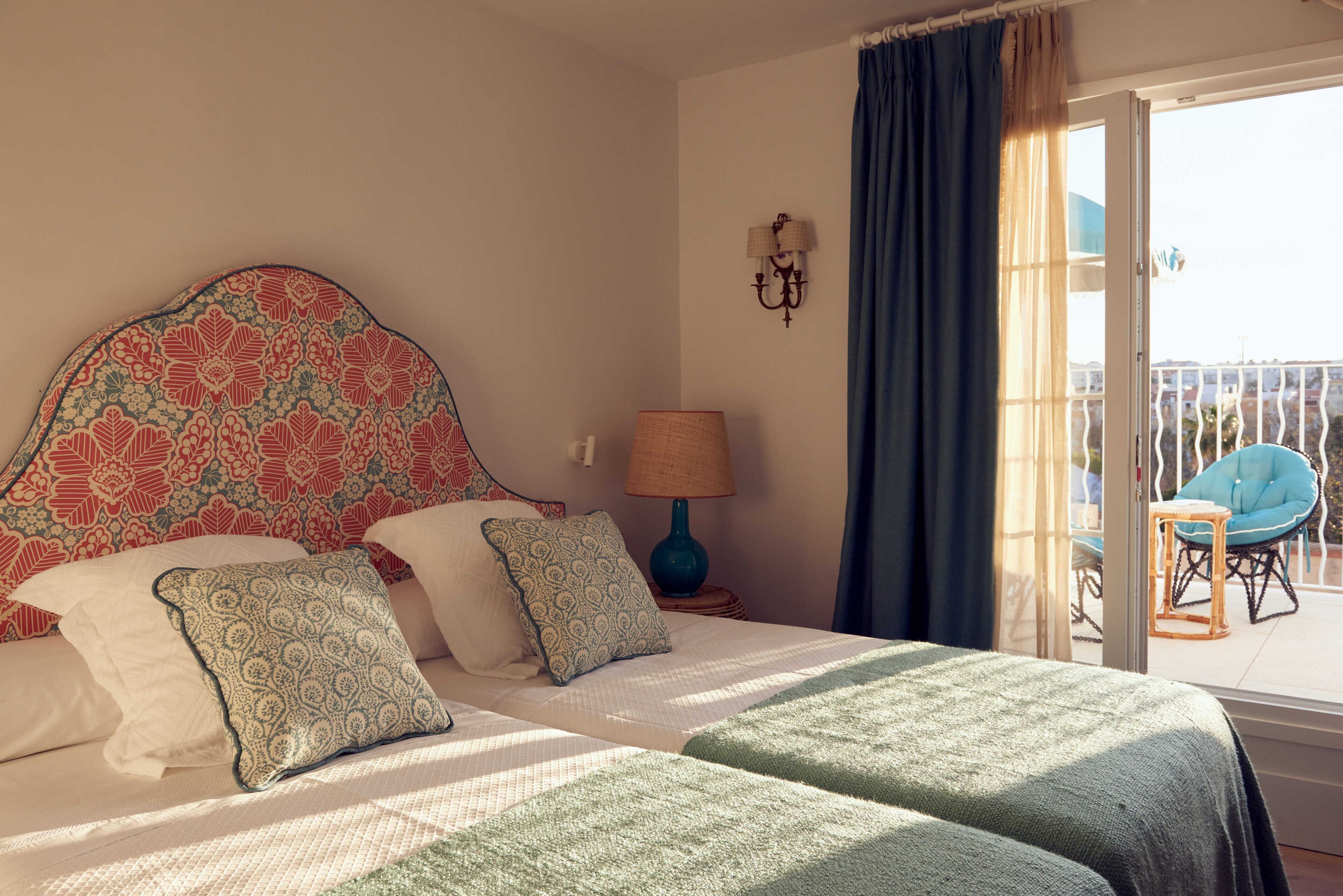 Habitación de hotel con cama, dos almohadas, lámpara, silla y vistas al exterior.