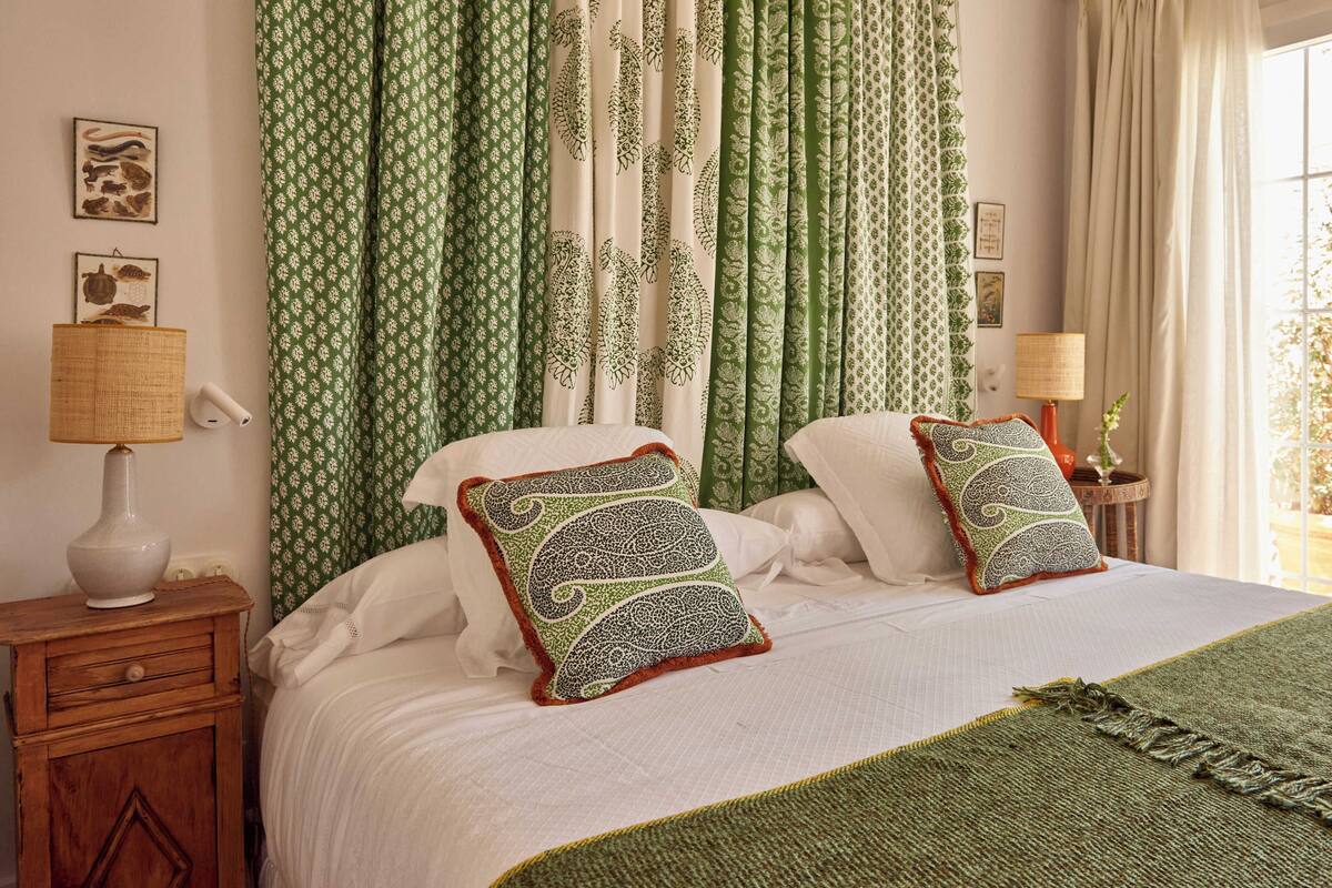 A bed with two decorative pillows, a bedside lamp, and a woven basket on a wooden nightstand.